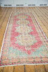 Distressed Oushak runner corner showing faded pink, blue, ivory Rococo floral and panel border.