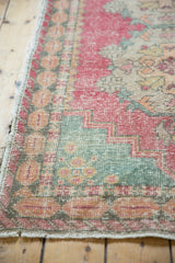 Distressed vintage Oushak rug corner, showing faded pink, green, and ivory tones with visible knot heads.