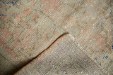 Distressed vintage Oushak pile with faint foundation, secured edge, and subtle pink-green hues.