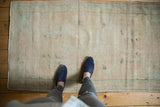 Distressed Oushak rug, pale beige with faded aqua floral motifs and worn texture, with feet.