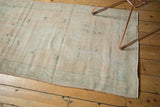 Distressed vintage Oushak rug end showing faded aqua green motifs on pale beige.