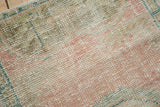 Distressed vintage Oushak rug showing texture of pale pink, ivory, deep green, and coffee tones.