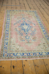 Secured side edge of distressed Oushak rug, revealing blue border and worn blush pile.