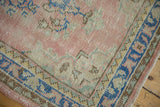 Distressed vintage Oushak rug corner, blush field, blue geometric border, faint foundation showing.
