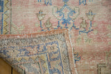 Vintage Oushak rug corner shows worn dusty blush pile, hand-knotted reverse, secured edge.
