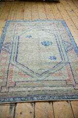 Distressed Oushak rug's lower edge showing worn pile and dusty blue-pink motifs.