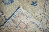 Distressed Oushak rug corner showcasing worn pile, blue secured edge, and woven foundation.