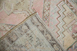Distressed Oushak rug corner showing worn blush, ivory pile, secured edge, and visible foundation.