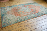 Textured distressed floral border in blue, mint green, and terra cotta of the Oushak rug.