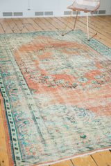 Distressed Oushak rug: terra cotta field, antique ivory border with sky blue floral vinery.