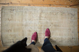 Distressed Oushak runner in antique ivory and pale coffee with faded floral design.