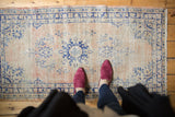 Overhead view of pink shoes on a vintage distressed Oushak rug, highlighting worn blush and navy patterns.