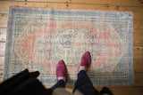 Distressed vintage Oushak rug featuring faded roundel medallion, pale rose field, and cobalt blue geometric border.