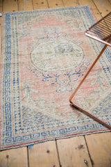 Distressed pale dusty rose Oushak field with even wear and cobalt blue patterns.