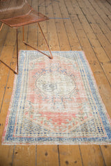 Distressed Oushak rug corner showing even wear, pale rose, and cobalt blue geometric border.