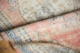 Distressed Oushak rug showing evenly worn pile, faded rose, ivory, and cobalt blue.
