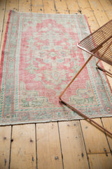 Distressed Oushak rug with pale raspberry, ivory, and mint, showing wear to foundation.
