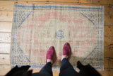 Distressed Oushak corner with cobalt blue geometric border and diamond lattice spandrel.