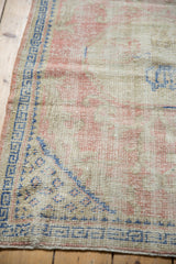 Vintage Oushak rug corner with cobalt blue geometric border and worn pale rose field.
