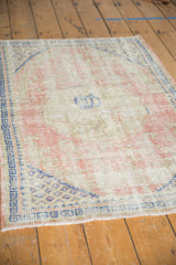 Distressed texture and visible foundation of a vintage Oushak rug with rose and blue geometric border.