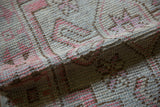 Folded distressed Oushak runner showing worn texture, silver, blush, and chocolate tones.