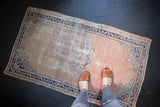 Distressed vintage Oushak rug with dusty rose and ivory field, cobalt blue accents, and textured wear.