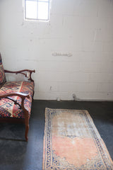 Distressed Turkish Oushak rug with a faded dusty rose field, low pile, and a cobalt blue vine border.