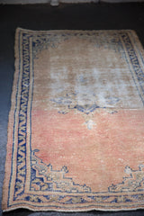 Distressed Oushak rug detail: cobalt blue meandering vine border, dusty rose field with mostly even wear.