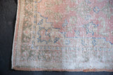 Vintage distressed Oushak rug corner showing worn pile in pale pink, beige, and blue with secured edge.