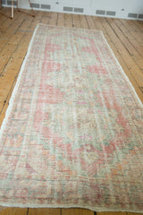 Distressed vintage Oushak runner texture with soft rose, ivory, and pale green hues.