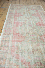 Distressed vintage Oushak runner with low pile and faded rose, ivory, green patterns.