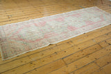 Distressed vintage Oushak runner's textured pile, displaying soft rose, ivory, and pale green.