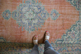 Distressed Oushak rug, pale orange rust abrashed field with worn blue-green palmette motifs.