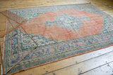 Distressed pale orange rust Oushak field with vibrant blue and green medallion fragments.