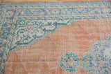 Distressed Oushak pile: abrashed pale orange rust field, foundation visible, palmette border.