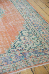 Distressed vintage Oushak rug corner, displaying pale orange rust field and patterned mint green border.