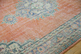 Distressed orange rust Oushak rug with abrashed field, visible wear, and vine border.