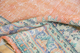 Distressed Oushak rug fold: pale orange rust field, foundation showing, green blue palmette border.