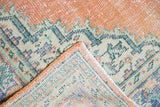 Distressed Oushak rug corner folded, revealing worn orange rust pile and mint green border.