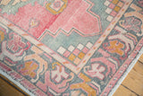 Distressed Oushak rug corner showing faded rose, sea-foam, and gold floral border.