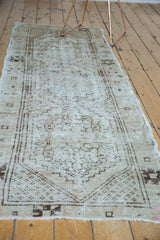 Distressed Oushak runner with faded primitive floral medallions and border in neutral tones.