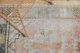 Distressed Oushak rug pile showcasing worn geometric and floral patterns with pale apricot and silver hues.