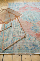 Distressed vintage Oushak carpet features pale brick red, aqua blue, and ivory vinery with low pile texture.