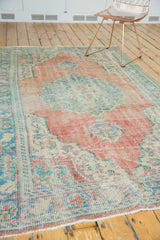 Distressed vintage Oushak rug corner showing faded brick red, ivory, and aqua tones with worn knot heads.