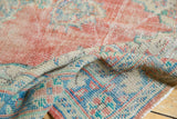 Distressed Oushak rug's folded texture with faded brick red, aqua, and ivory tones.