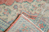 Distressed Oushak rug corner showing worn knot heads, blush, aqua, and secured edges.