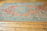 Distressed Oushak rug showing worn pile and muted blush, aqua, and ivory patterns.
