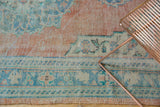 Distressed vintage Oushak carpet border showing pale brick red, aqua, and denim blue geometric patterns.