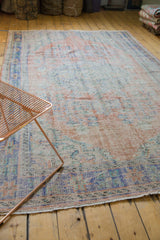 Distressed Oushak carpet with faded apricot, royal blue, and mint green floral motifs.