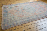 Distressed Oushak rug corner, revealing secured edge, even wear, and faded blue and apricot tones.